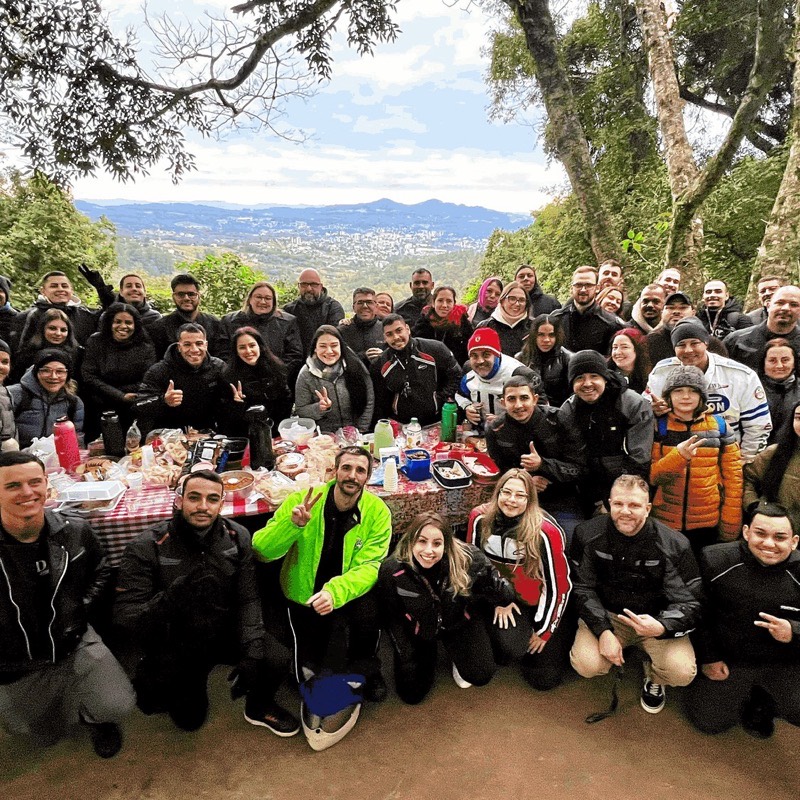 Dezenas de integrantes do Los Bravos reunidos em volta de uma mesa de café da manhã em um mirante na serra